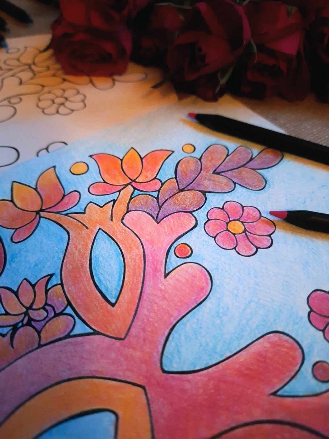 Colorful tree of life drawing on paper with flowers and leaves, surrounded by red roses.